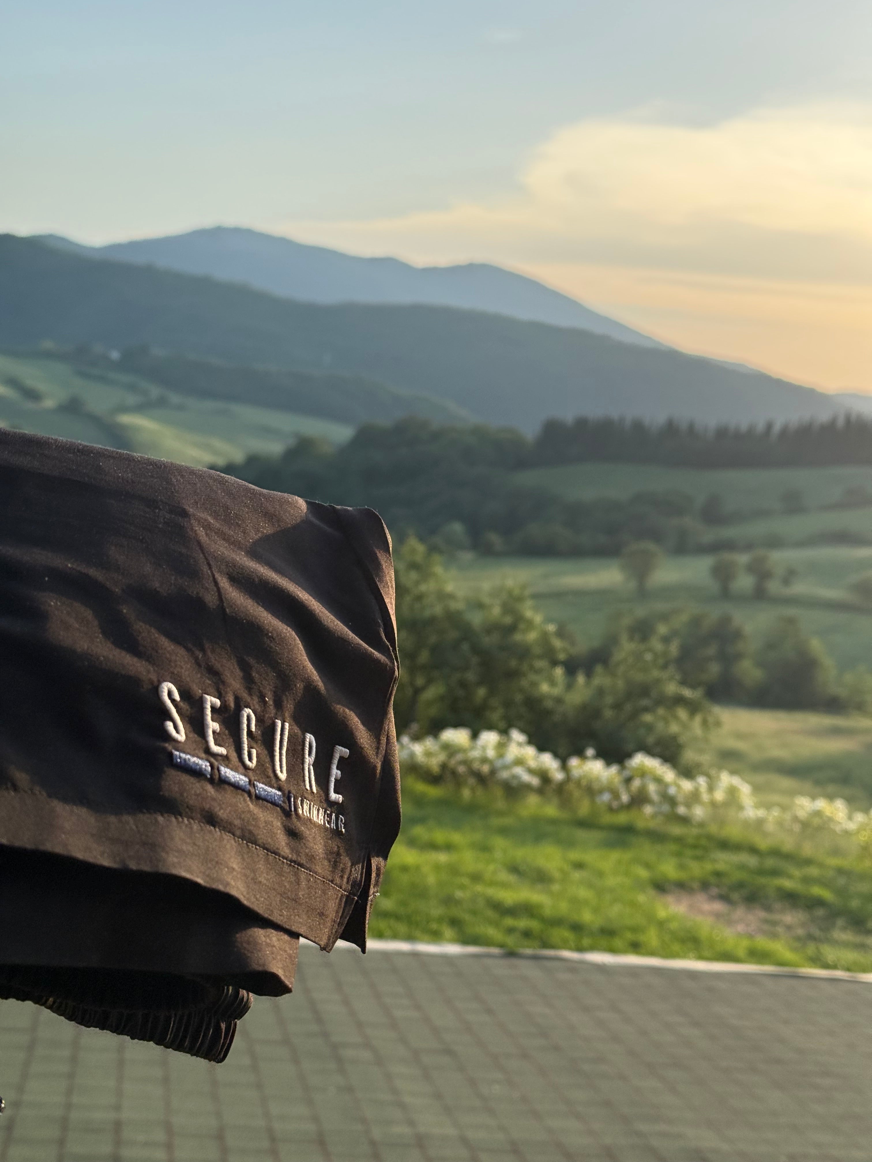 black secure swimwear waterproof swim shorts with a hidden snapshut waterproof pocket overlooking a scenic countryside and mountain landscape