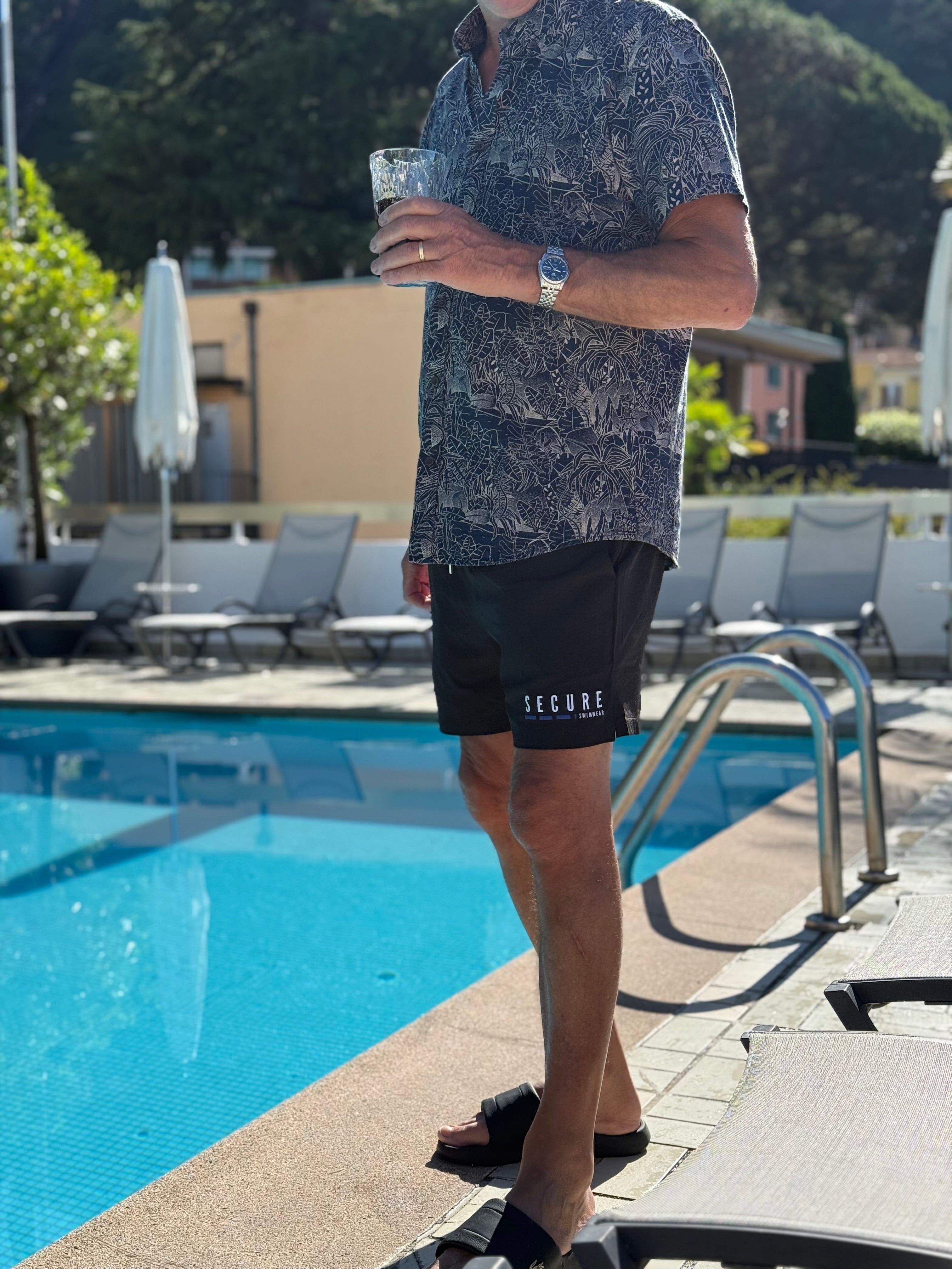 man wearing black secure swimwear waterproof swim shorts with a hidden snapshut waterproof pocket beside a luxury swimming pool
