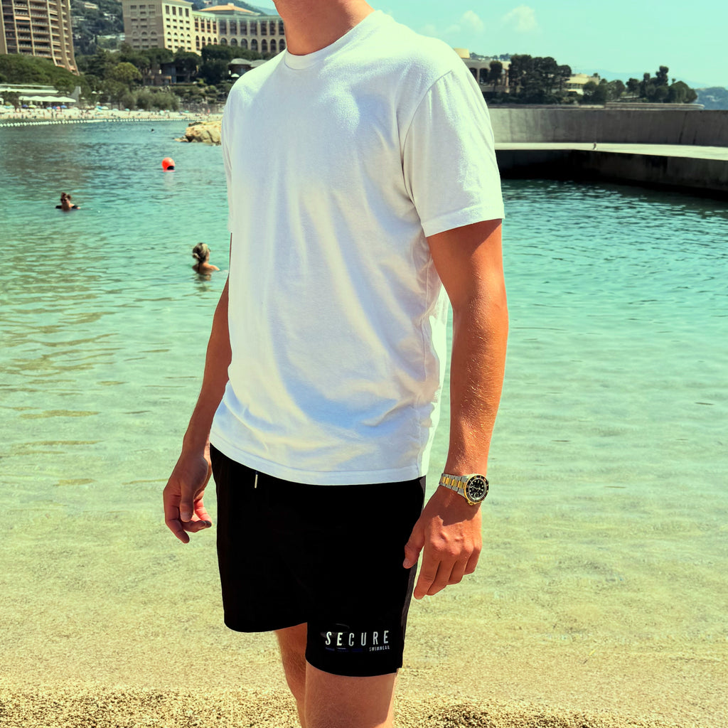 man wearing black secure swimwear waterproof swim shorts with a hidden snapshut waterproof pocket on a beach by the sea